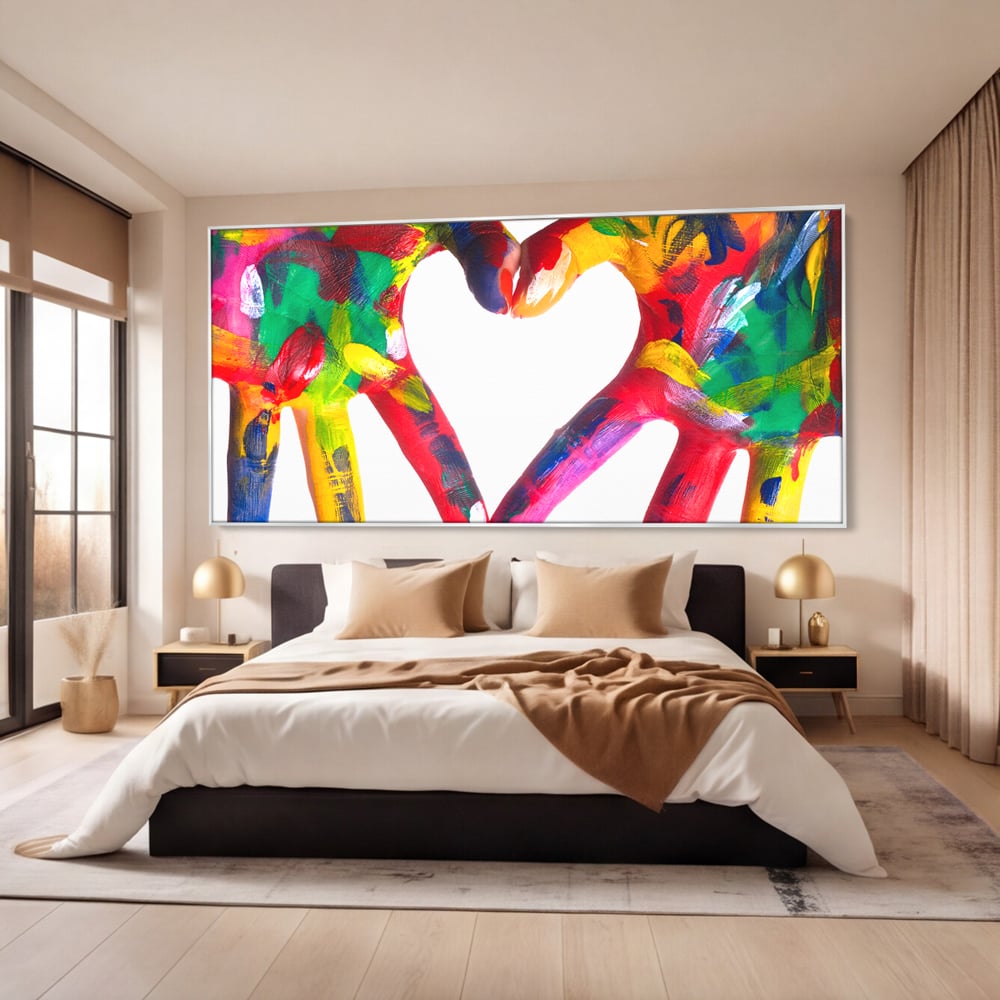 Tablou canvas cu pictura cu maini colorate formand o inima, in rama de aluminiu argintiu, pe perete intr-un dormitor